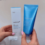 Hand holding Medicube Zero Foam Cleanser tube with packaging box in the background