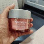 Hand holding Neutrogena Bright Boost Night Cream jar showing pink gel texture and silver lid