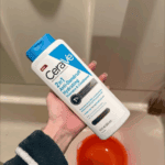 Hand holding CeraVe Anti-Dandruff 2-in-1 Hydrating Shampoo and Conditioner 355ml bottle in bathroom sink area for dandruff relief and scalp hydration in Sri Lanka