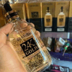Hand holding a Dr Rashel 24K Gold Radiance and Anti-Aging Primer Serum bottle with visible gold flakes, photographed inside a cosmetics shop with boxed Dr Rashel 24K Gold products displayed on shelves in the background.