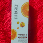 Dr Rashel Vitamin C Brightening & Anti-Aging Whitening Cream box for private parts, featuring orange vitamin C graphics on white packaging, placed on a red textured background.