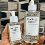 Hand holding 50ml and 100ml SKIN1004 Madagascar Centella Tone Brightening Capsule Ampoule bottles side by side