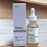 The Ordinary Lactic Acid 10% + HA 30ml serum in a frosted glass dropper bottle displayed beside its white product box on a wooden surface.