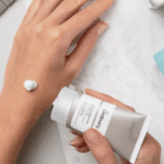 Hands dispensing The Ordinary Natural Moisturizing Factors + HA 30ml moisturizer from a grey tube with a small amount of cream applied on the back of the hand.