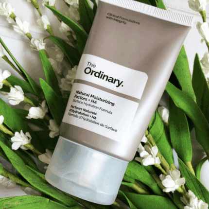 The Ordinary Natural Moisturizing Factors + HA 30ml grey moisturizer tube placed among green leaves and small white flowers.