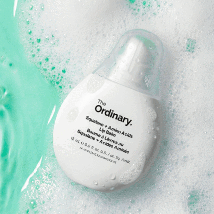 The Ordinary Squalane + Amino Acids Lip Balm 15ml in a white teardrop-shaped bottle placed among water and foam bubbles with a fresh aqua background.