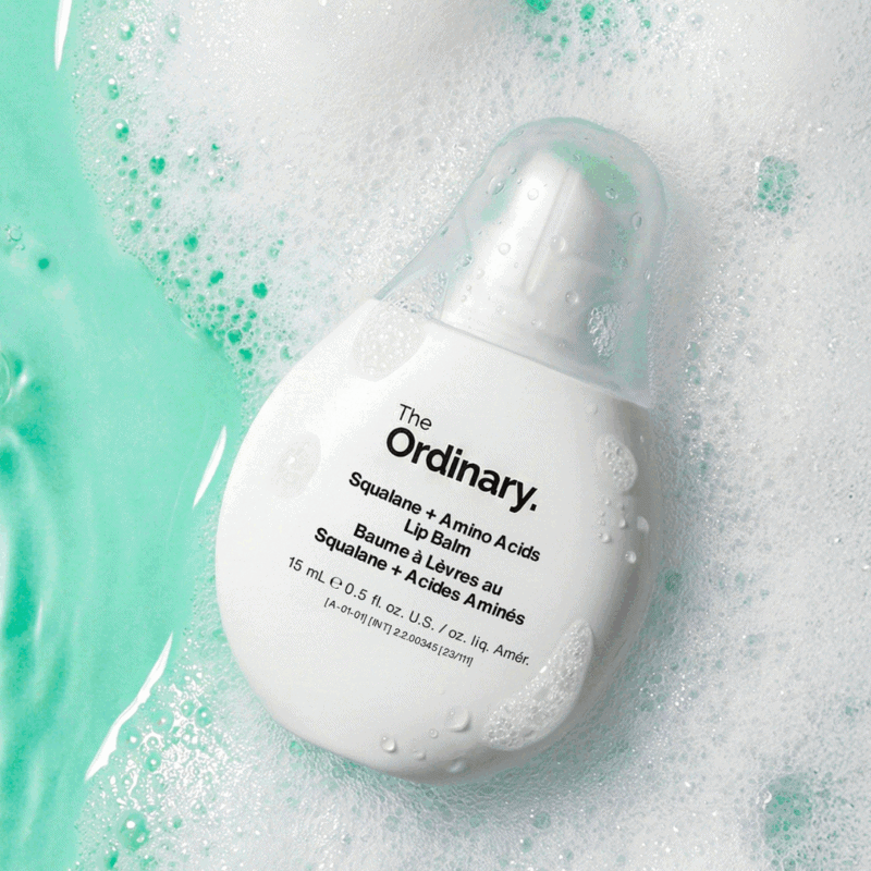 The Ordinary Squalane + Amino Acids Lip Balm 15ml in a white teardrop-shaped bottle placed among water and foam bubbles with a fresh aqua background.