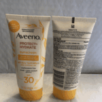 Front and back view of an Aveeno Protect + Hydrate SPF 30 sunscreen tube displayed upright against a neutral background, showing the product label on the left tube and the ingredient and drug facts panel on the right tube.