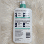 Back view of CeraVe Foaming Facial Cleanser bottle showing ingredients, usage instructions, and product details on a white pump bottle with green cap placed on a soft fur background