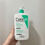 Hand holding a CeraVe Foaming Facial Cleanser white pump bottle with green label, designed for normal to oily skin, shown against a plain background for a real-life skincare usage view