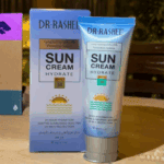 DR.RASHEL Sun Cream Hydrate SPF 50 tube placed in front of its packaging box on a table, showcasing sunscreen for UV protection and hydration in a real-life setting with warm lighting