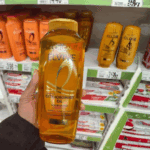 Hand holding L’Oréal Elvive Extraordinary Oil nourishing shampoo bottle in a retail store aisle with hair care products on shelves in the background, showcasing a product for dry and dull hair