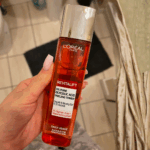 Hand holding L’Oréal Revitalift 5% Pure Glycolic Acid peeling toner in a bathroom setting, showcasing an exfoliating skincare product designed to brighten and smooth skin