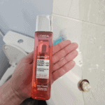 Hand holding L’Oréal Revitalift 5% Pure Glycolic Acid peeling toner in a bathroom setting, showcasing an exfoliating skincare product designed to brighten and smooth skin
