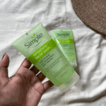 Hand holding two Simple Refreshing Facial Wash gel tubes on a soft fabric background, showcasing a gentle cleanser for sensitive skin in a natural lifestyle setting