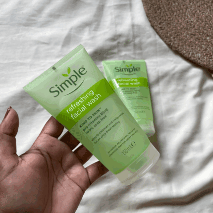 Hand holding two Simple Refreshing Facial Wash gel tubes on a soft fabric background, showcasing a gentle cleanser for sensitive skin in a natural lifestyle setting