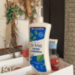 St. Ives Renewing Collagen and Elastin body lotion pump bottle placed on a bathroom shelf with skincare items and decor in the background, showcasing a hydrating and skin-firming lotion in a real-life setting