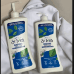 Two St. Ives Renewing Collagen and Elastin body lotion pump bottles placed on soft white fabric, showcasing moisturizing and skin-firming skincare products in a clean lifestyle setting