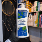 Gloved hand holding St. Ives Renewing Collagen and Elastin body lotion pump bottle in a store setting with skincare products in the background, showcasing a hydrating and skin-firming lotion